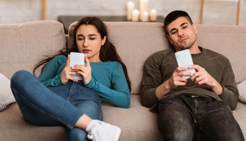 Couple zoned out in the lounge ignoring each other whilst on their phones.