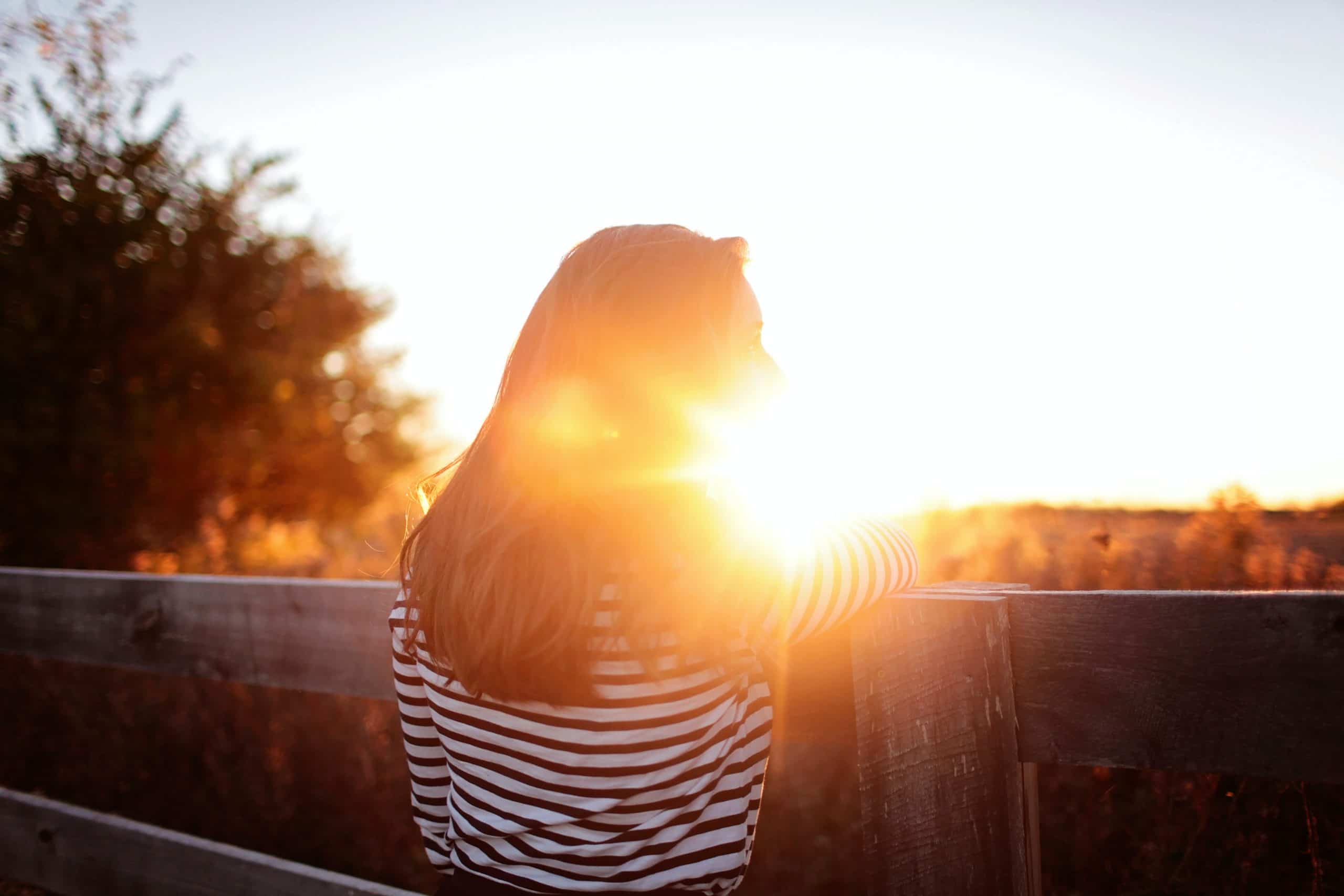 Woman standing on a balcony looking out at a sunset.