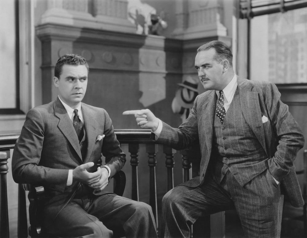 An old fashioned photograph of two men in suites one is pointing at the other