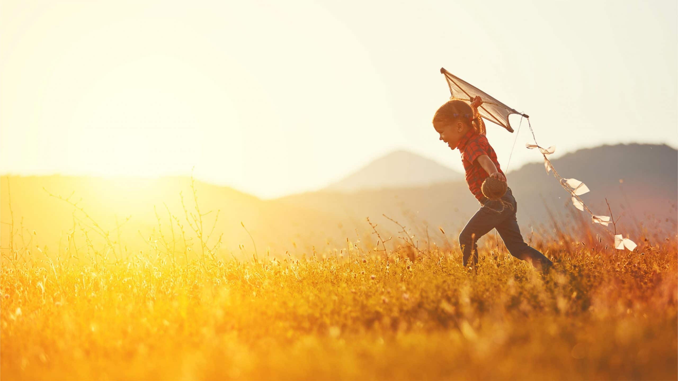 A child running with a kite in a meadow.