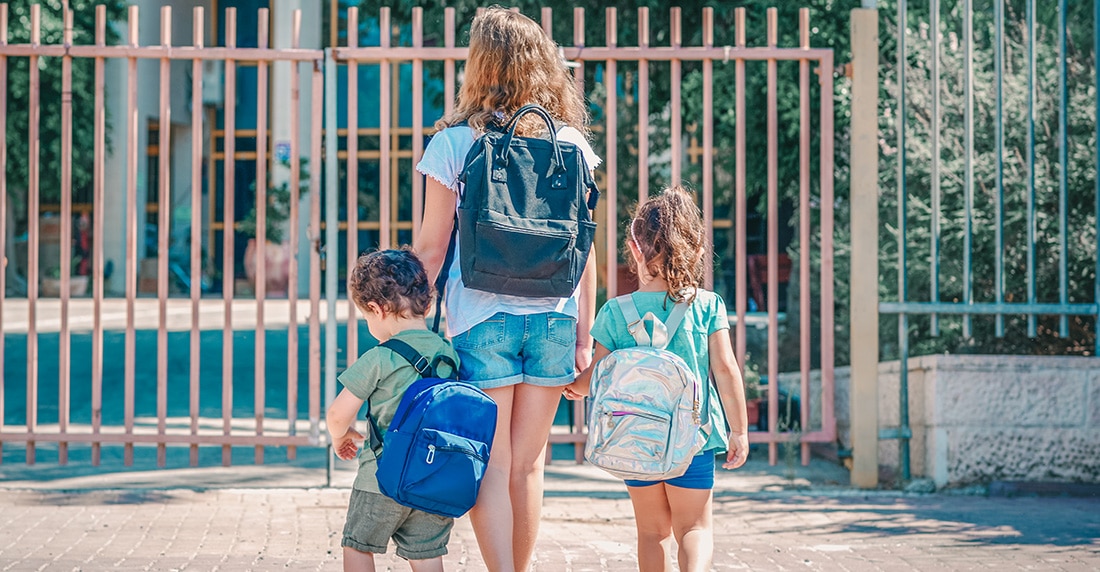 Young mother holding the hands of her two children as she walks them to school