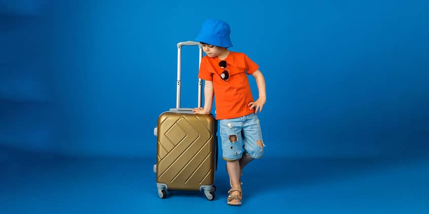 Small child standing with a suitcase who looks dressed for a holiday