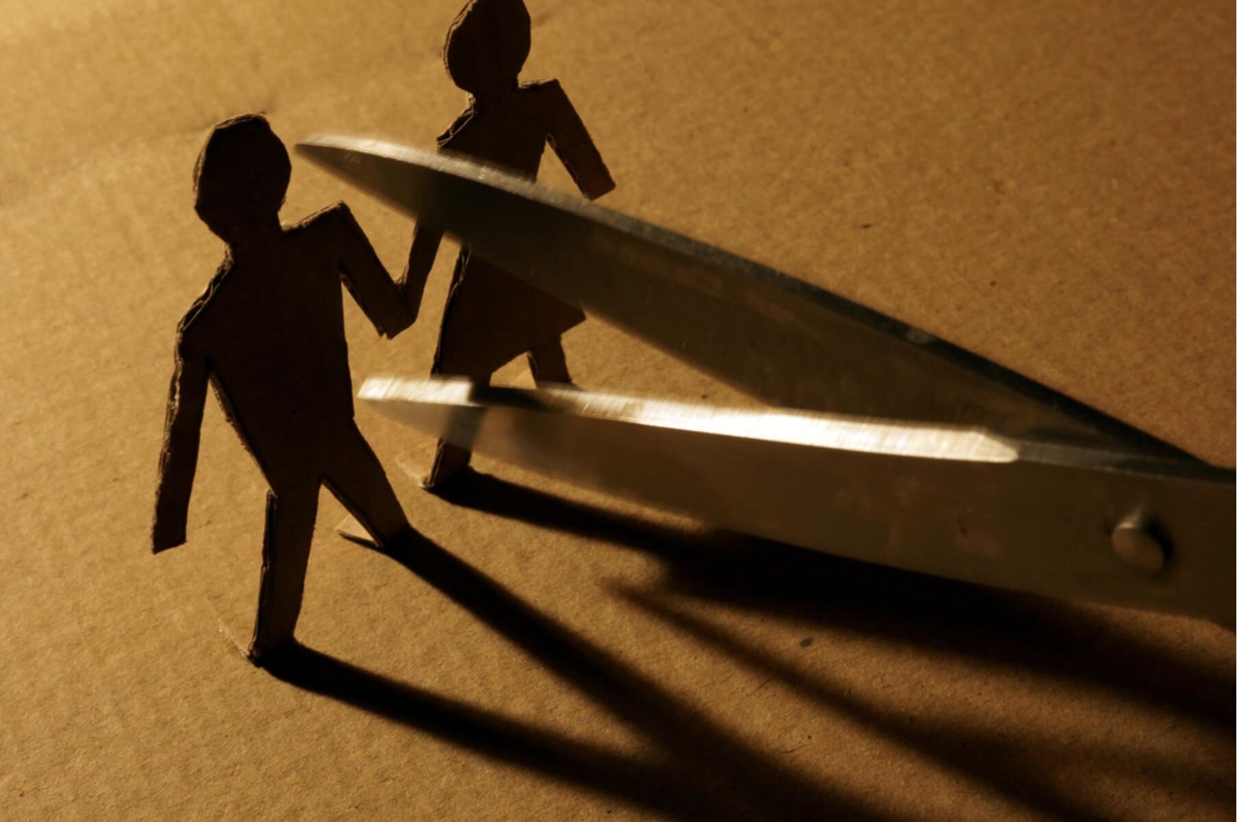 Scissors cutting a cardboard cutout of a man and woman representing a couple separating.