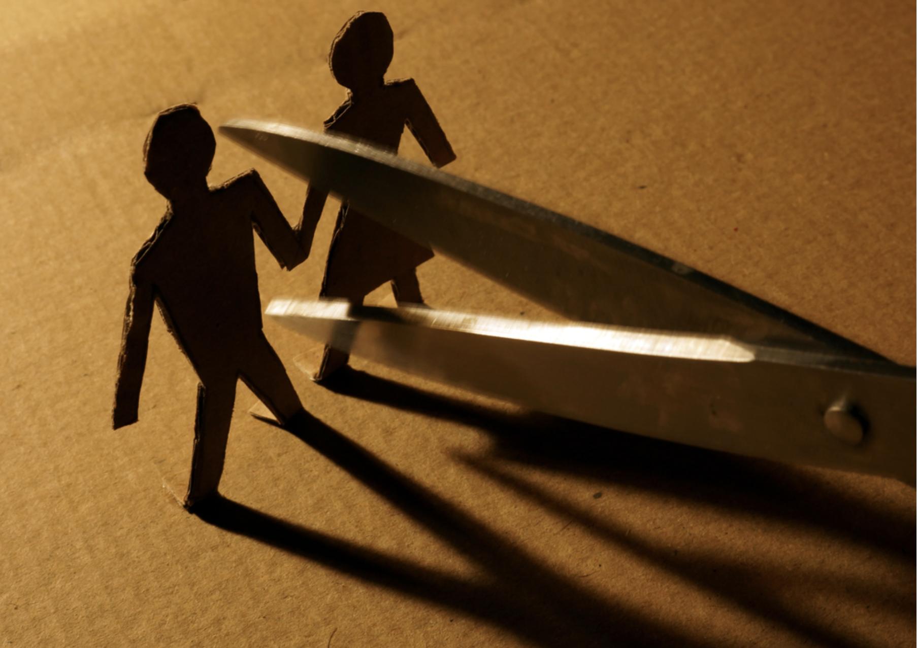 Scissors cutting a cardboard cutout of a man and woman representing a couple separating.