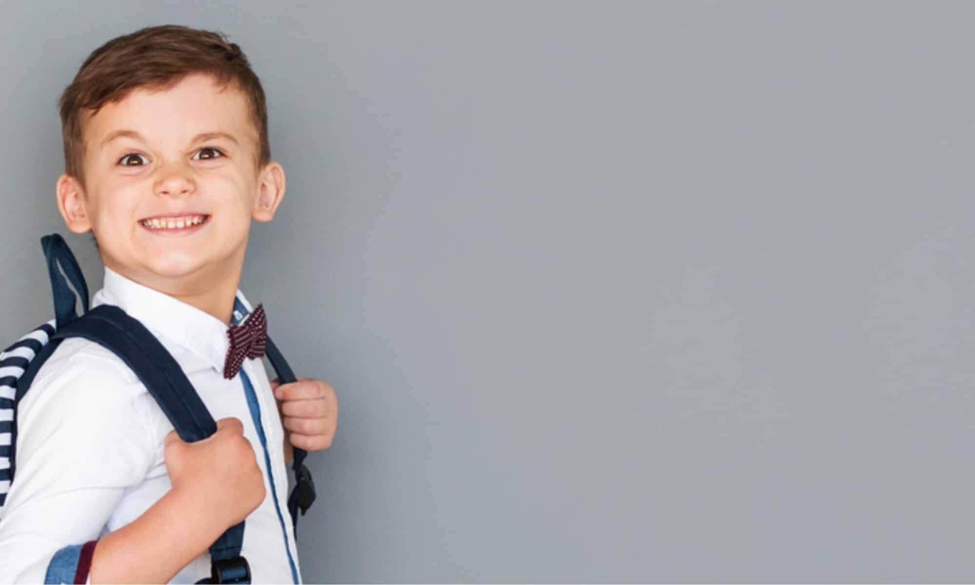 Smiling, happy child in uniform wearing a school backpack.