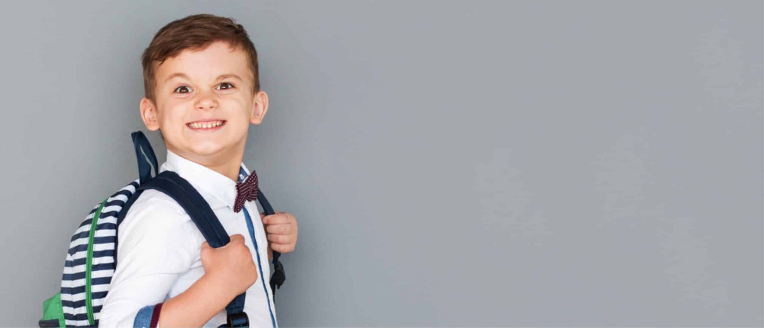 Smiling, happy child in uniform wearing a school backpack.